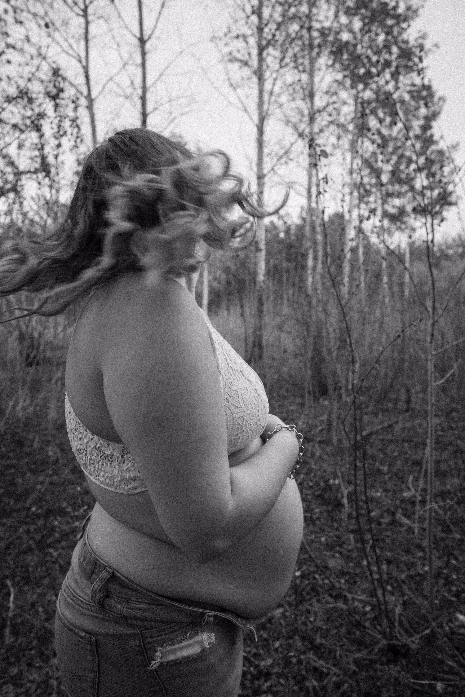 Black and white maternity portrait showing silhouette against wooded background.