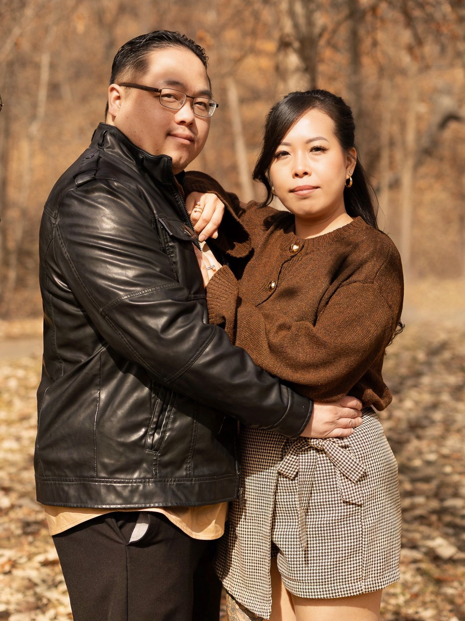 Romantic couple in autumn setting wearing leather jacket and brown coat pose together outdoors.
