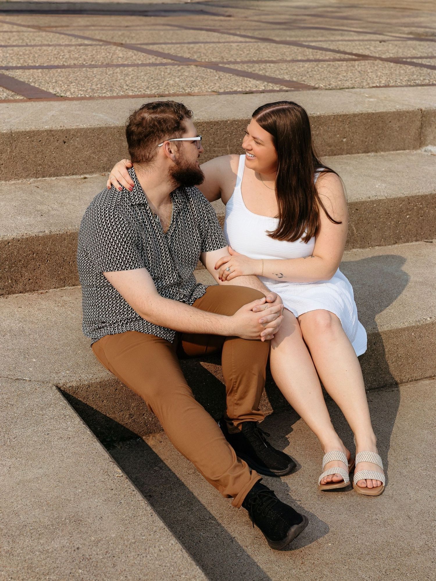 A couple sitting and talking on concrete steps during a sunny afternoon.
