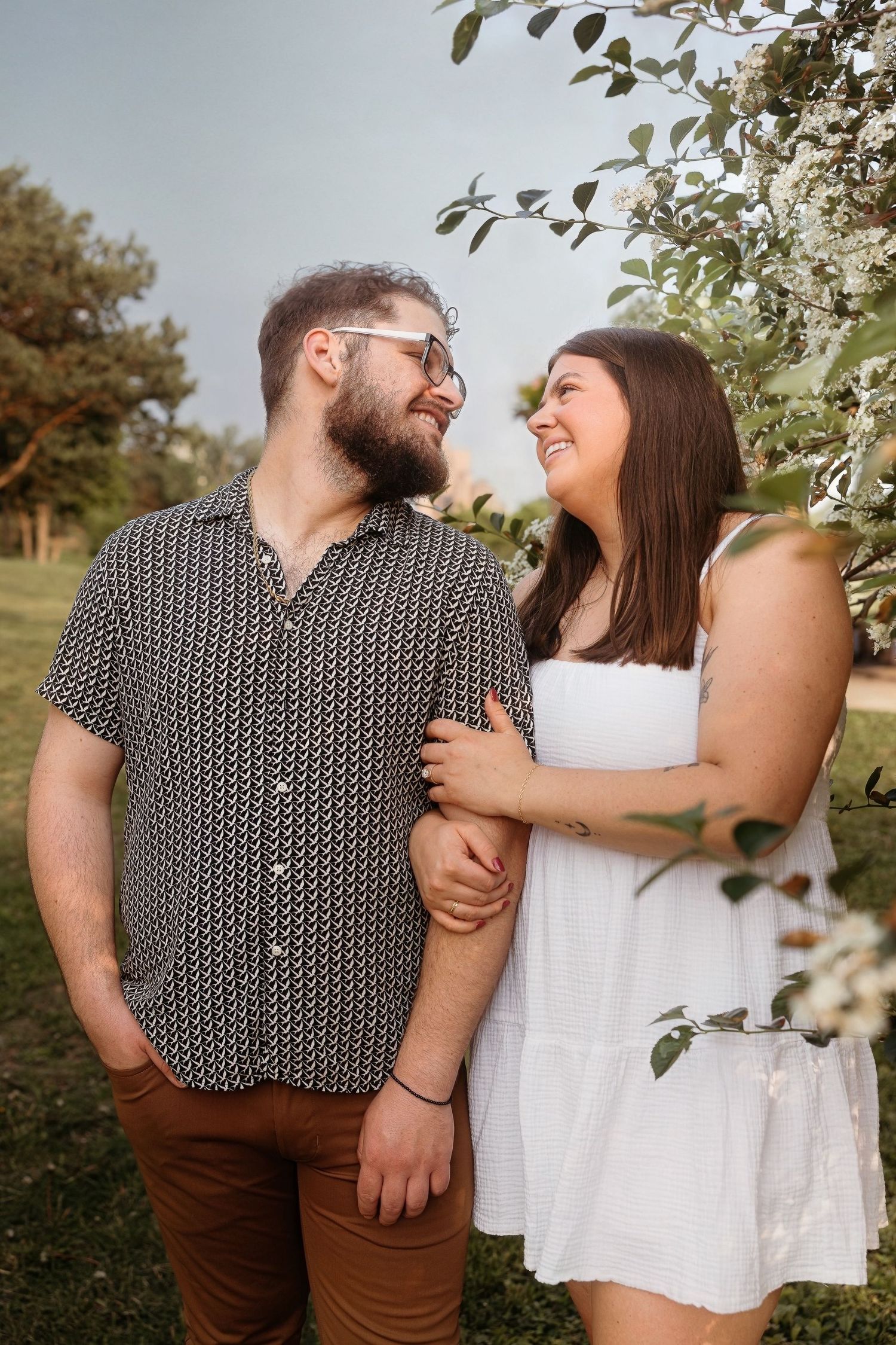 A romantic outdoor portrait of a couple in casual attire sharing a joyful laugh together in a natural garden setting.