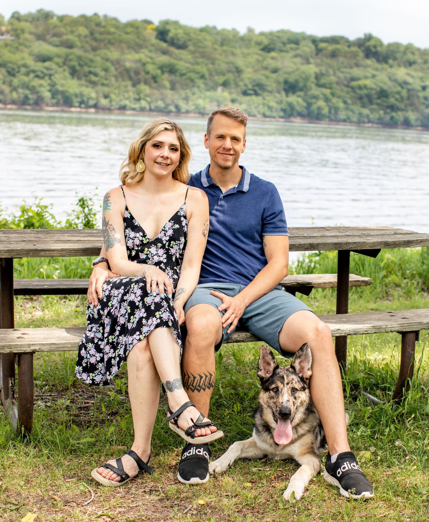 Couple sitting on wooden bench by lake with their German Shepherd dog.