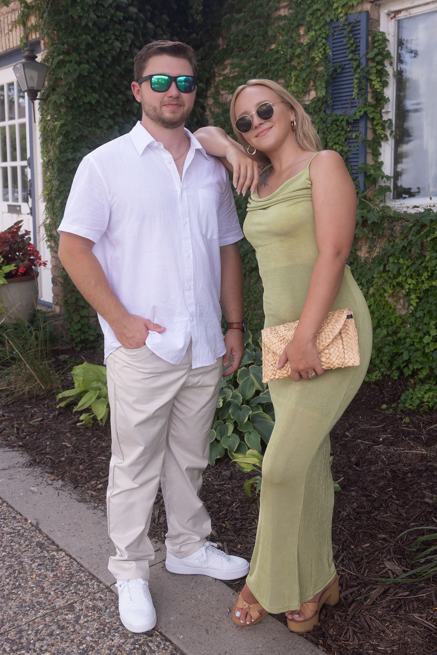 A couple in matching white and yellow summer outfits poses together in an outdoor garden setting.