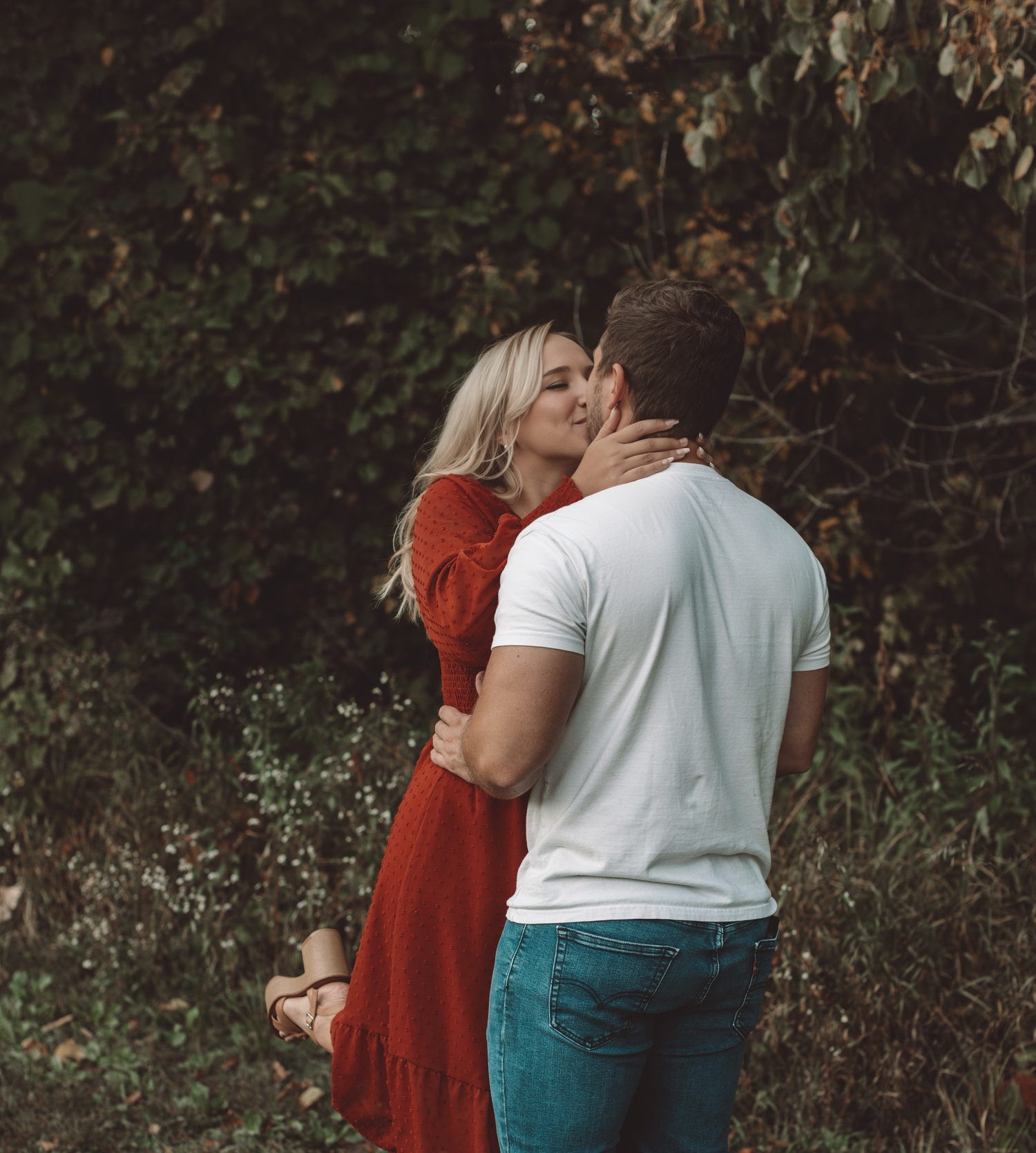 Intimate couple portrait with person in red dress and white shirt against natural backdrop.
