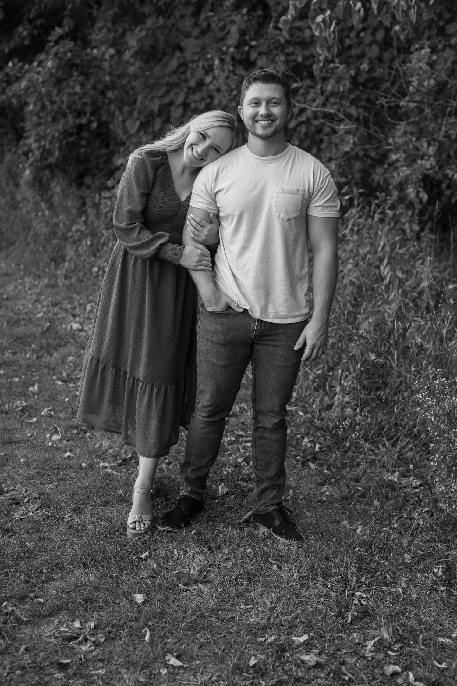 Black and white photo of couple posing together against natural foliage.