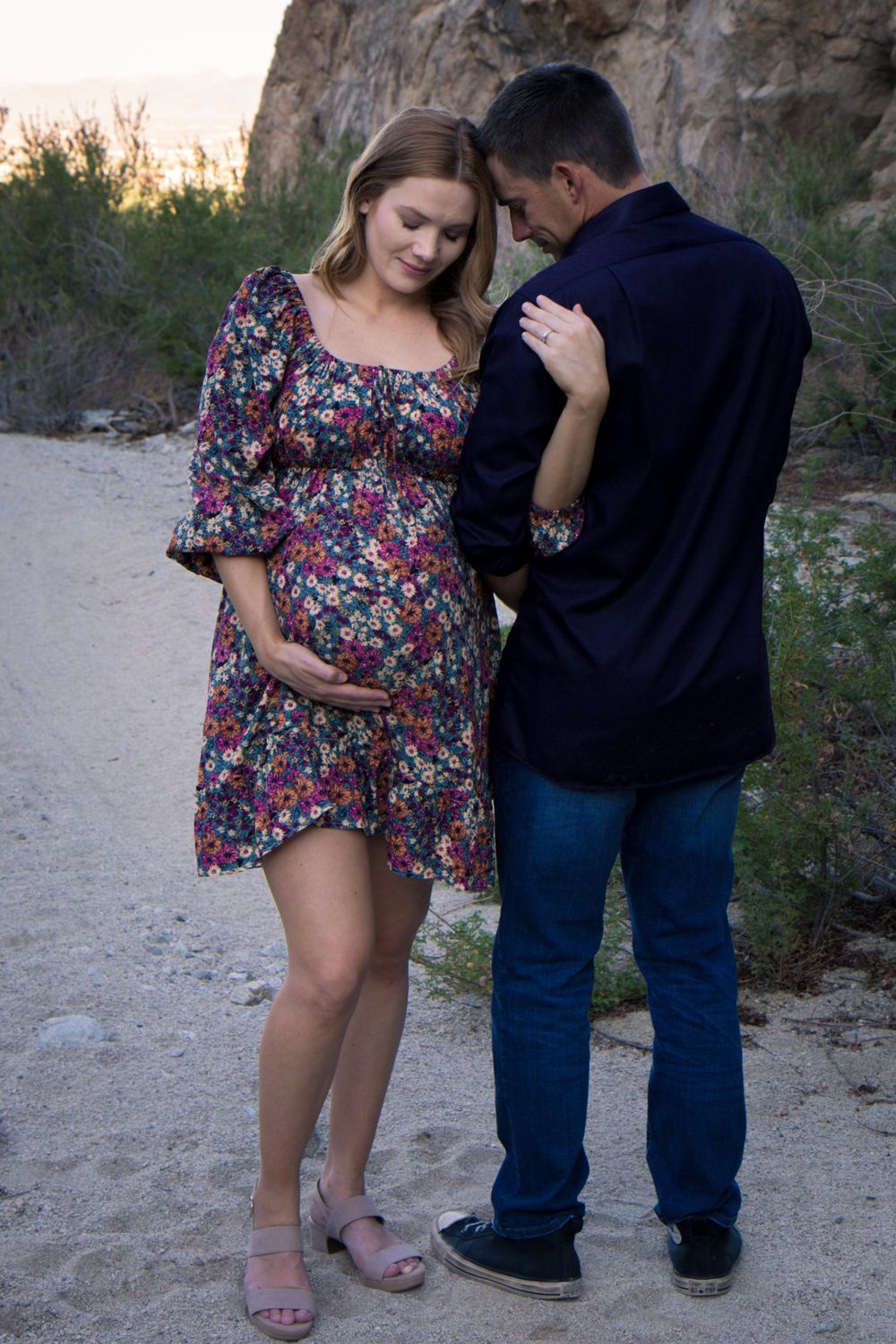 A couple in casual attire share an intimate moment together on a sandy path during sunset.