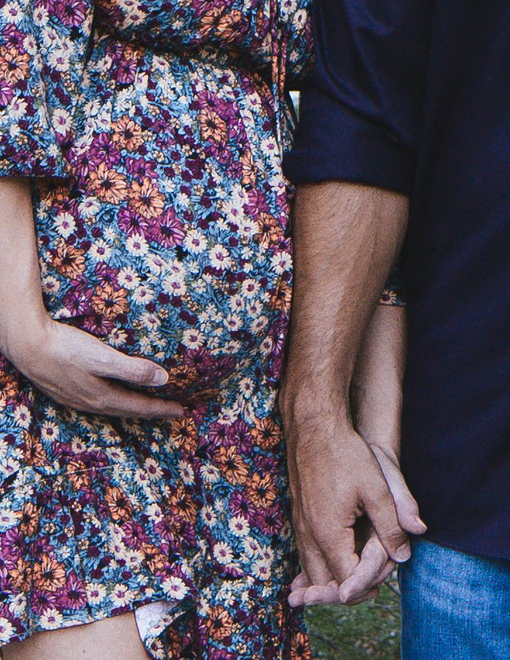 A couple holding hands wearing floral print and navy blue clothing against a colorful floral backdrop.