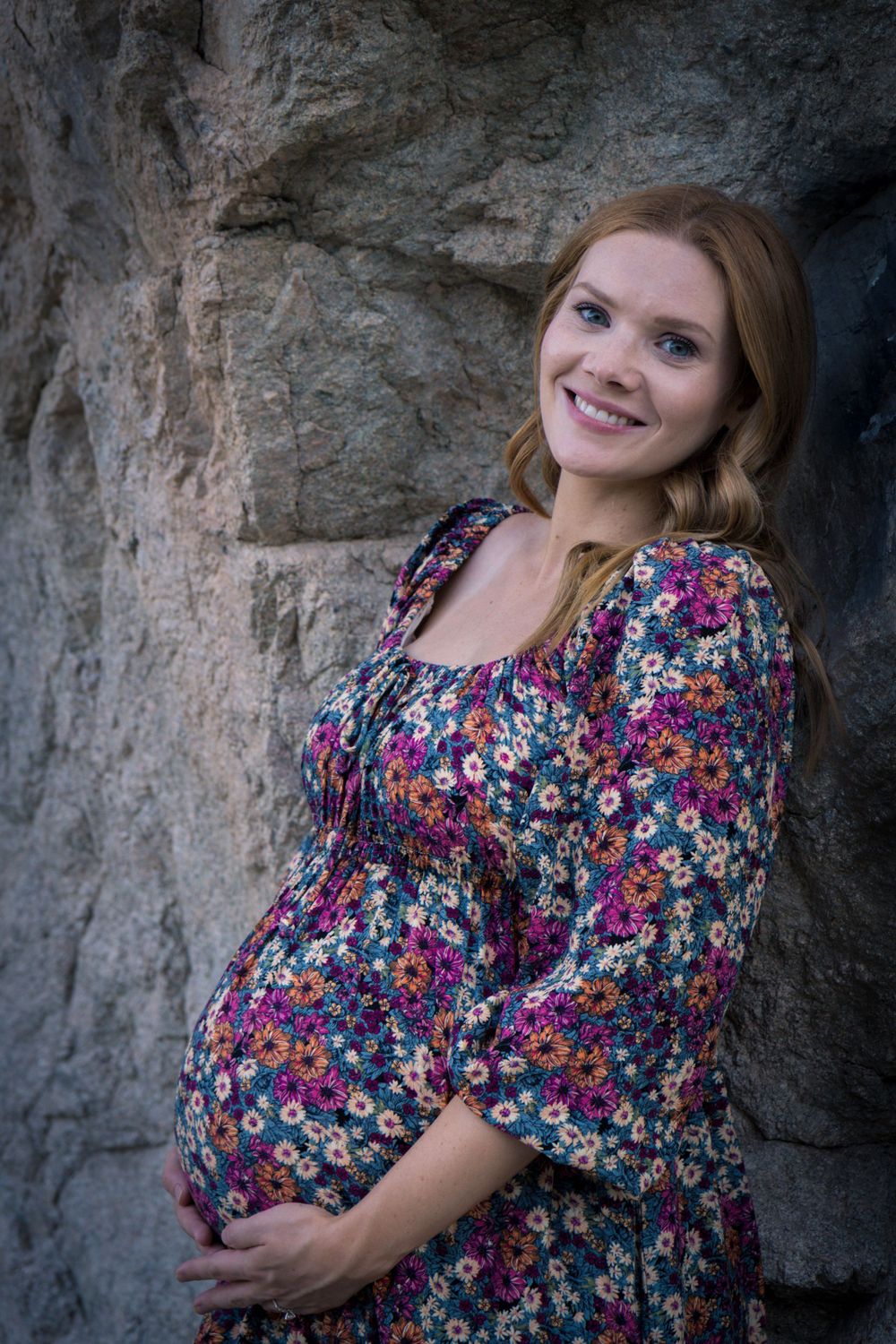 A person in a floral print dress poses against a textured stone wall in a series of artistic portrait shots.