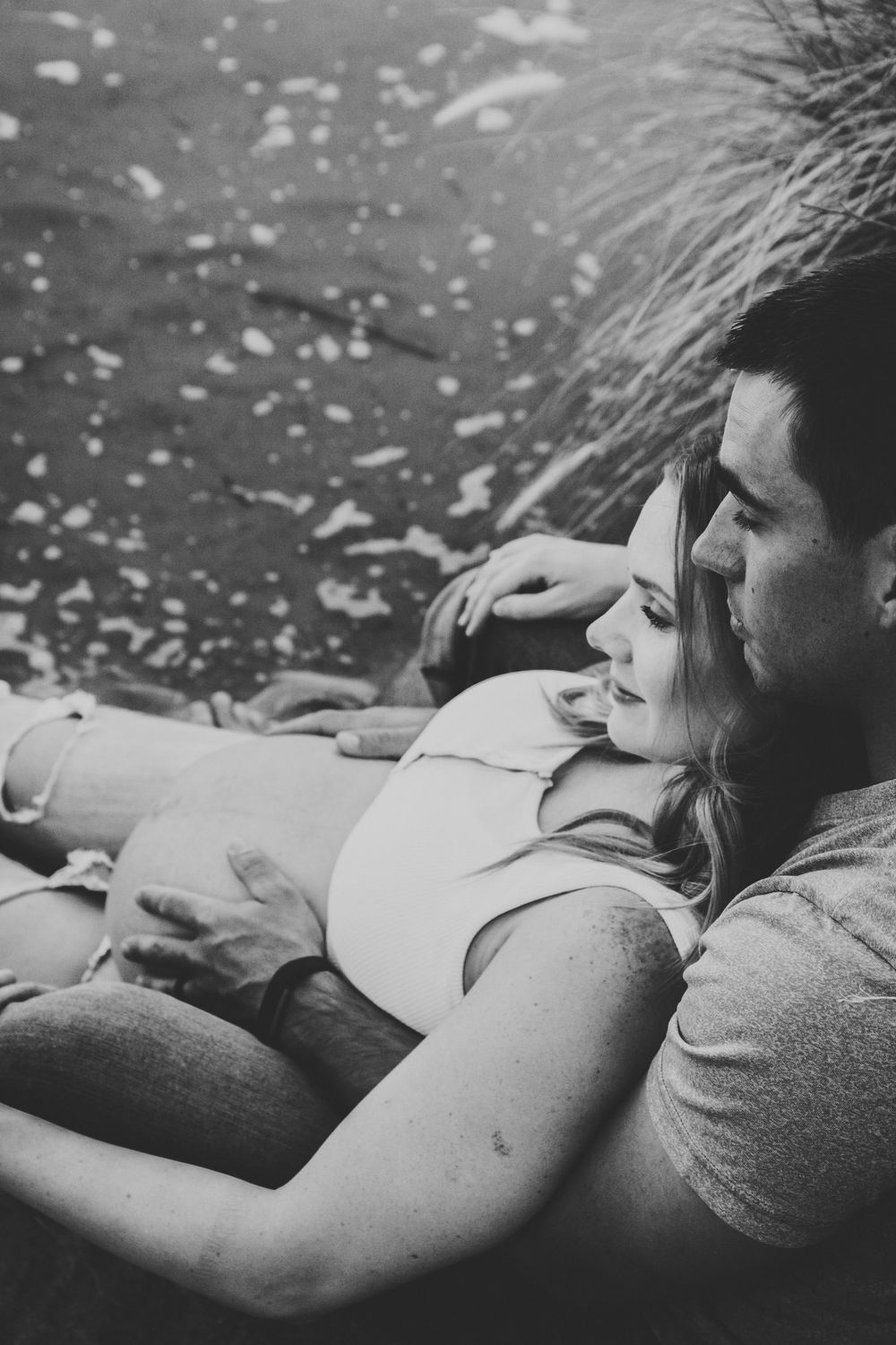 A couple lying together in a tender black and white moment, resting peacefully against each other.