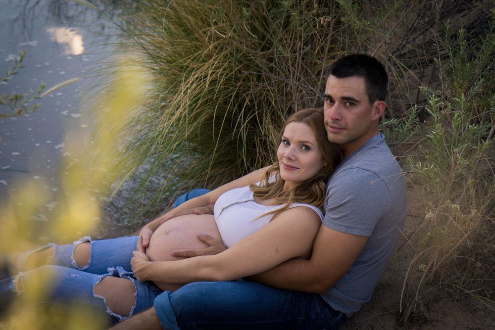 A couple sits together outdoors during a romantic sunset photoshoot in a natural setting.
