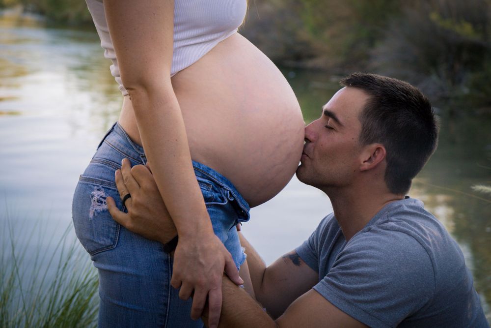 A tender pregnancy photo shoot by a lake shows an intimate moment between expectant parents at sunset.