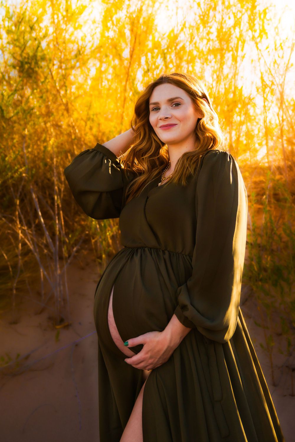 A maternity photoshoot in a black dress against golden autumn trees during sunset creates a warm, ethereal glow.