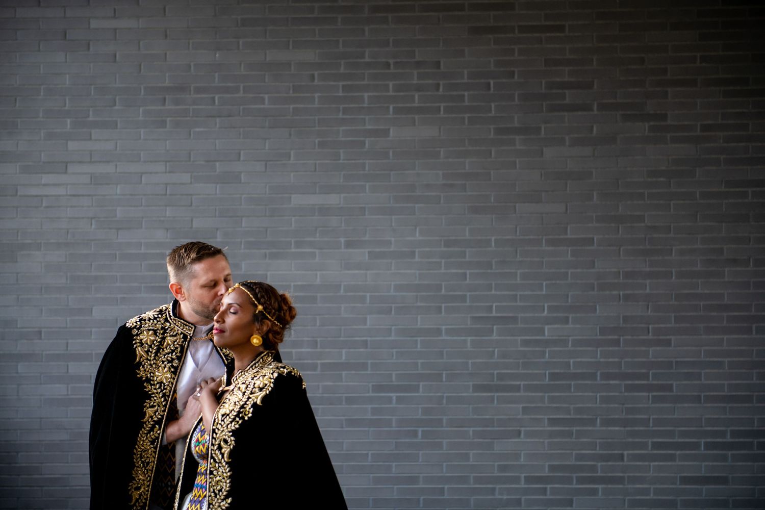 Artistic wedding portrait in traditional Ethiopian dress against industrial brick wall background.