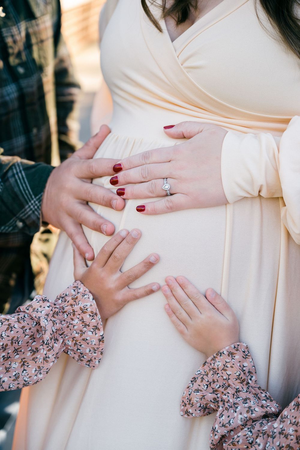 Close-up shots of hands wearing an engagement ring against a cream-colored maternity dress with floral sleeve details.