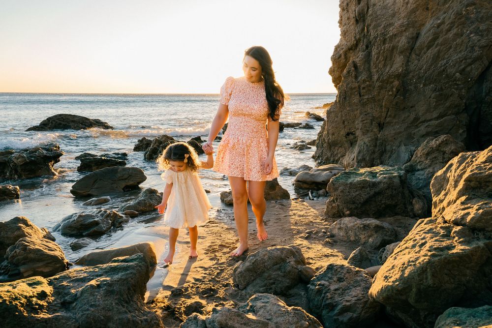 Silhouettes of people walking along rocky beach coastline during golden sunset hour.