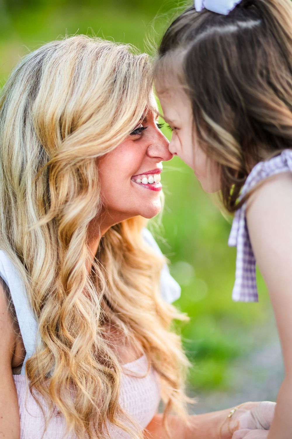 A candid image of a mother and daughter touching noses smiling.