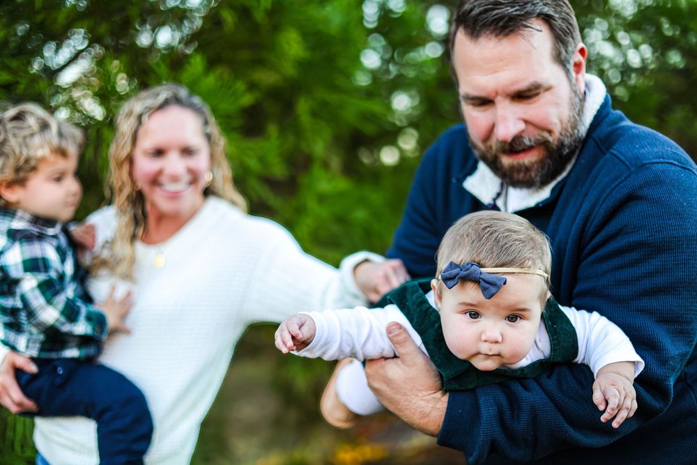 A lifestyle image of a family playing together in the winter. A mother is holding her son while her husband is holding their baby girl.