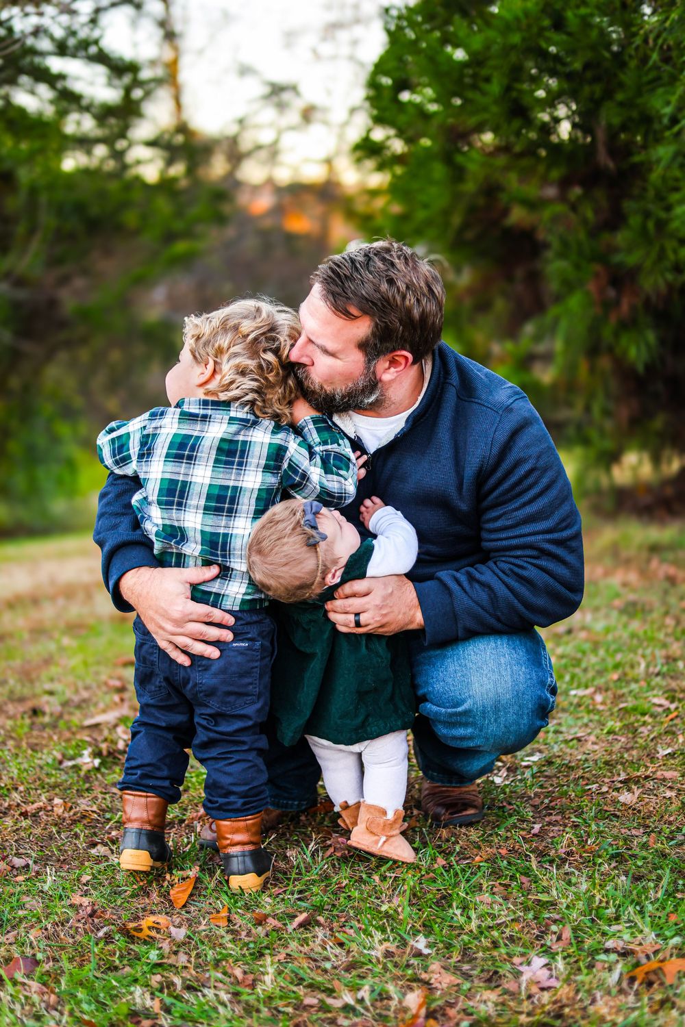 A lifestyle image of a father bending down to hug/ hold his two children, a little boy and a baby girl in the Winter.