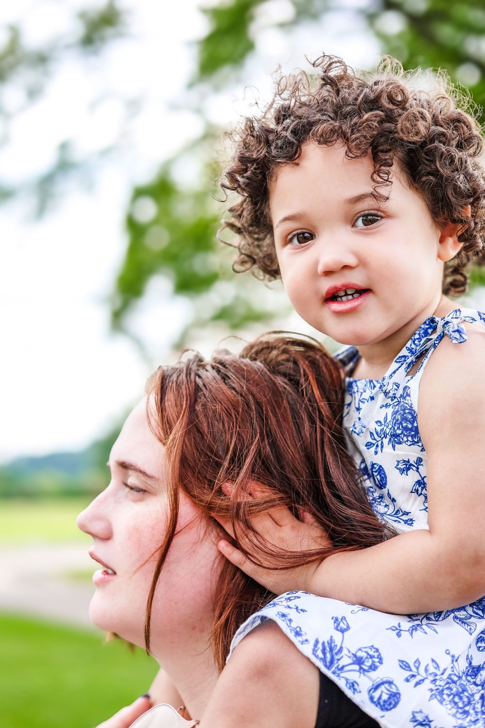 A candid lifestyle image of a mother giving her baby daughter a ride up on her shoulders looking off in the distance.