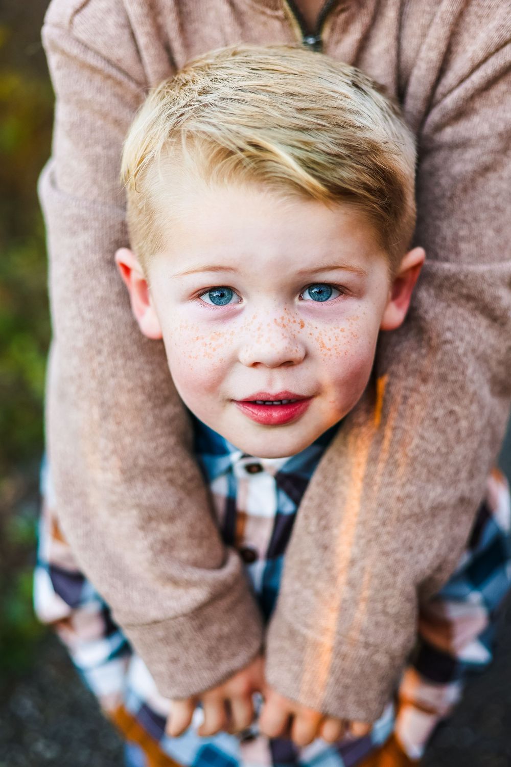 A lifestyle close-up image of a young boy being hugged by his brother from behind while looking up at the camera curiously.