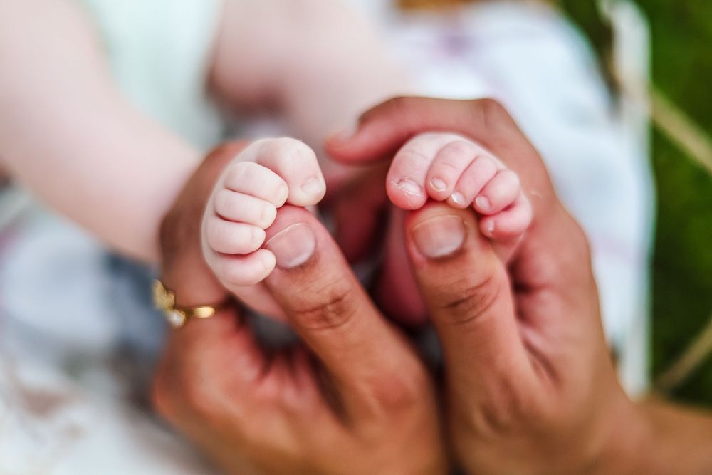 A lifestyle picture of a close up crop image of baby feet being held in hands.