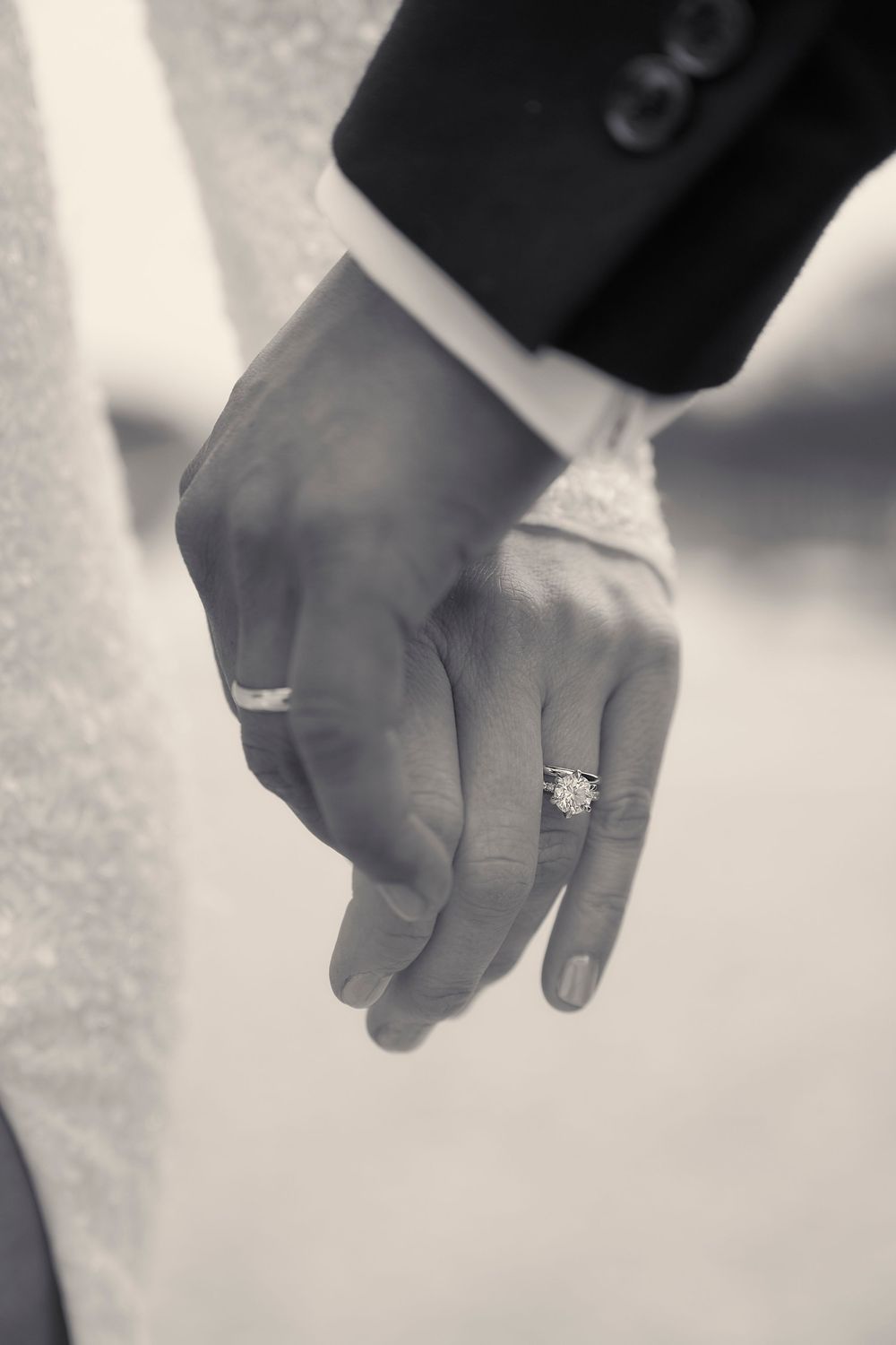 Three black and white close-up images of hands wearing engagement rings and wedding bands.