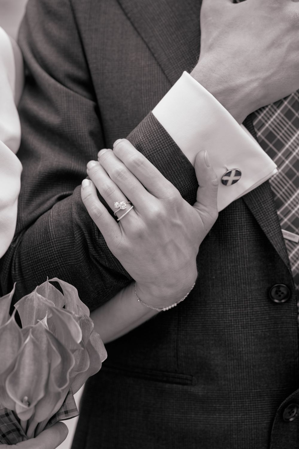 Black and white close-up of suit sleeves and cufflinks showing wedding ring details.