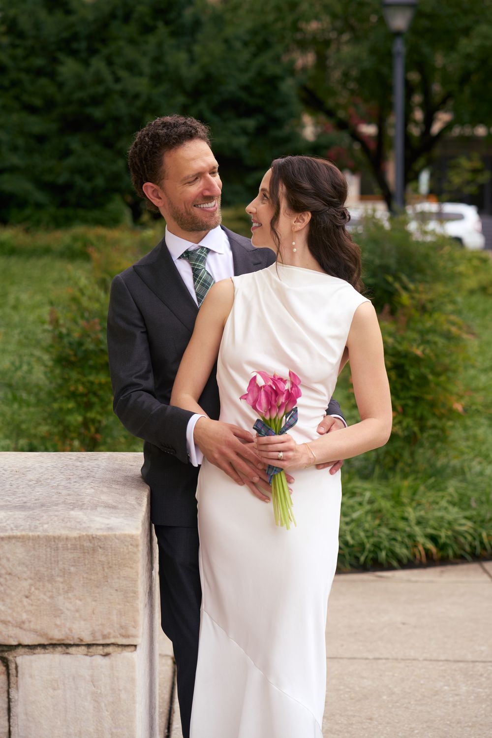 A couple embraces outdoors on their wedding day with bride in white dress holding colorful bouquet.
