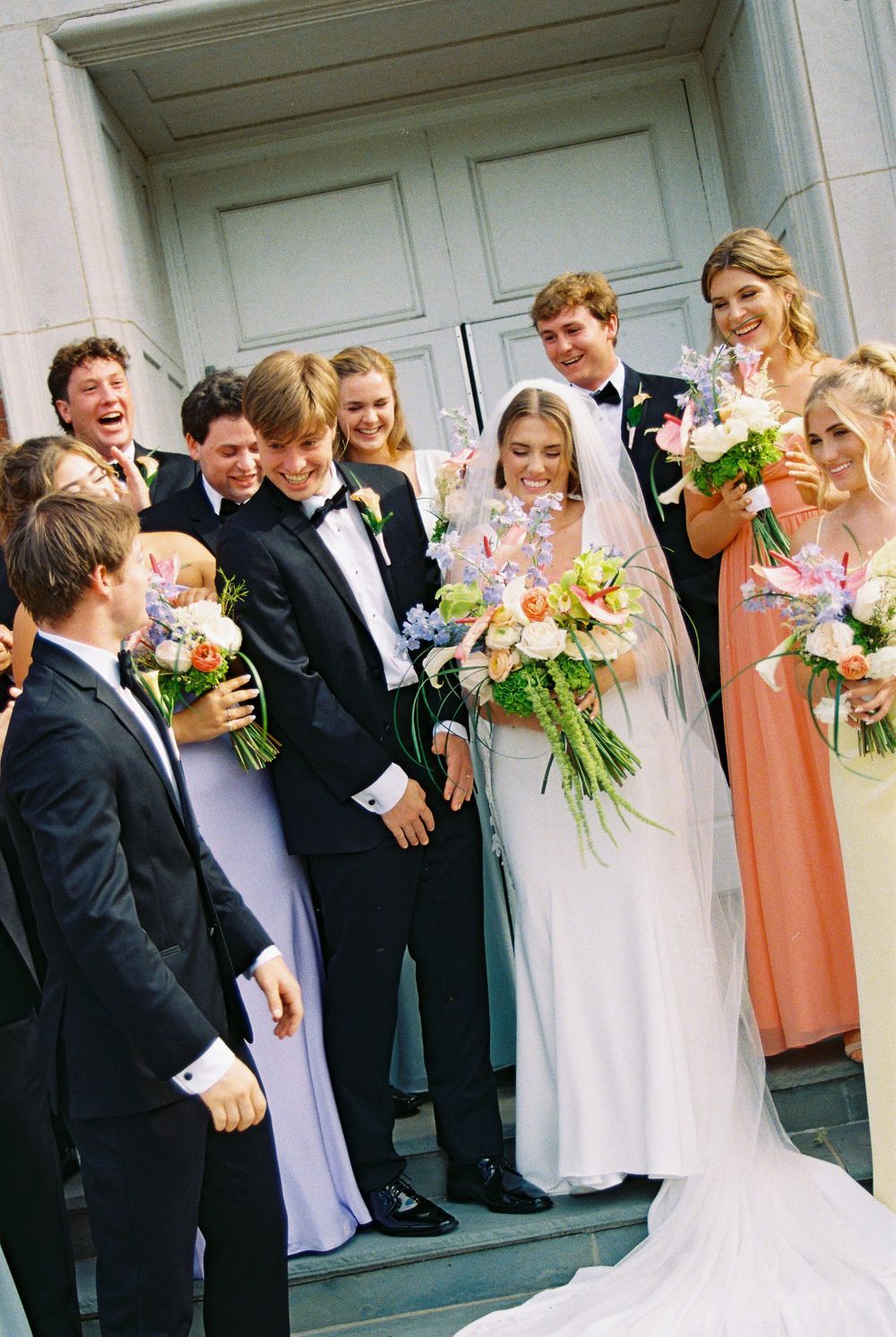 Wedding party poses for candid photos outside a white building in a fun and playful sequence.