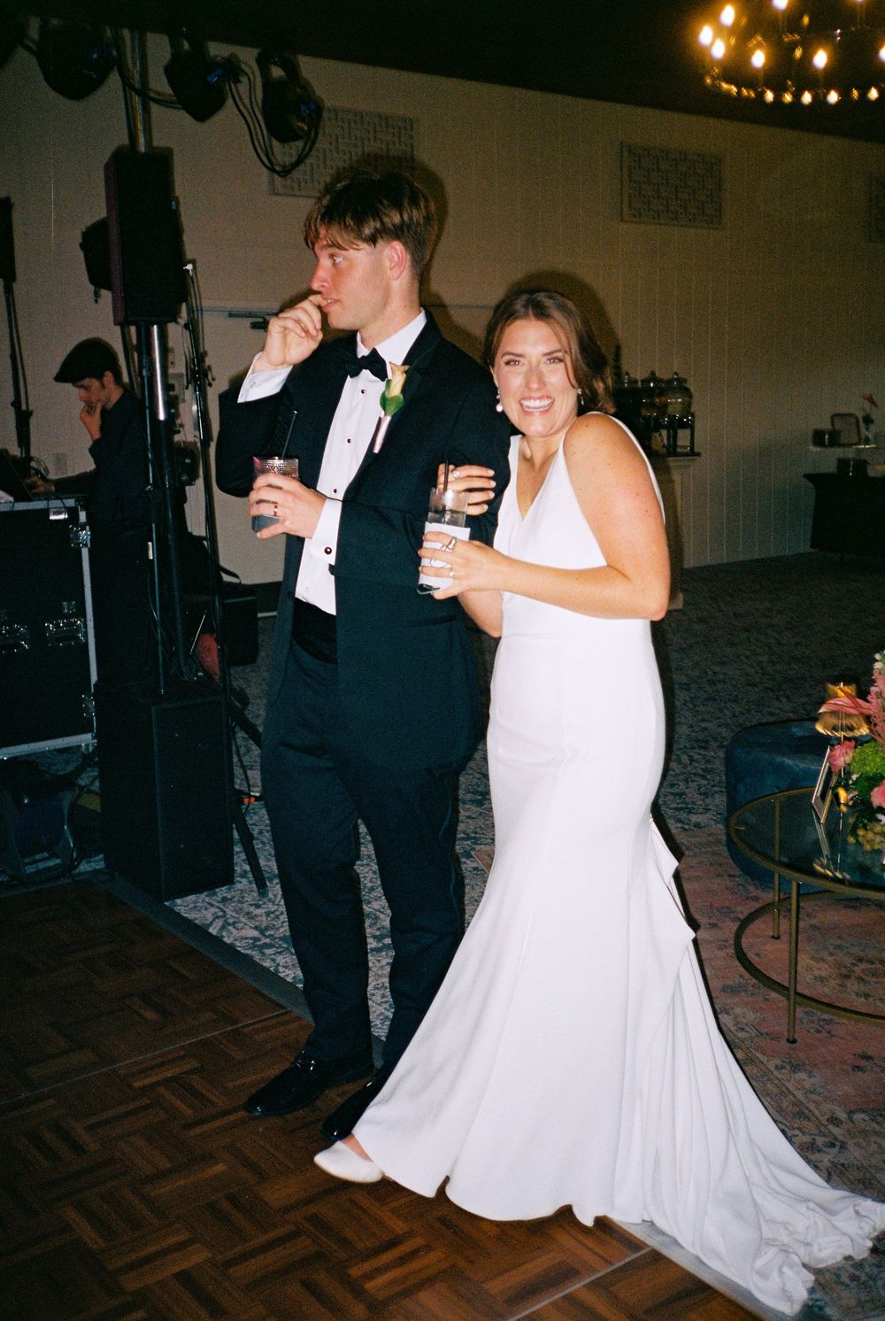 A couple dances together at a wedding reception on a parquet dance floor under soft lighting.