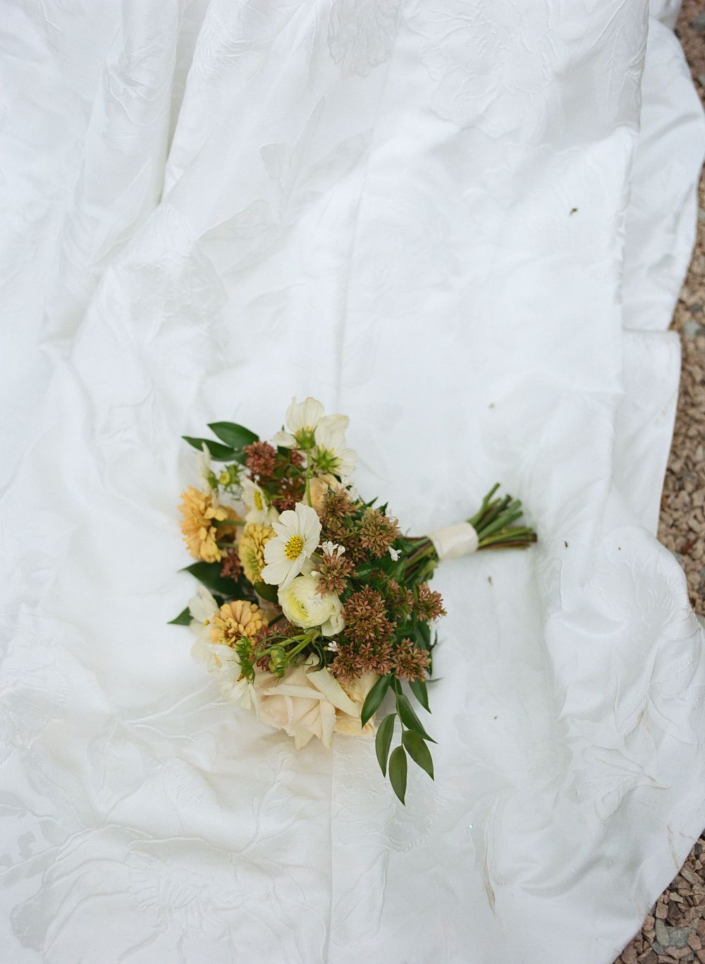 A white linen fabric background with a delicate floral arrangement featuring white blossoms and greenery.
