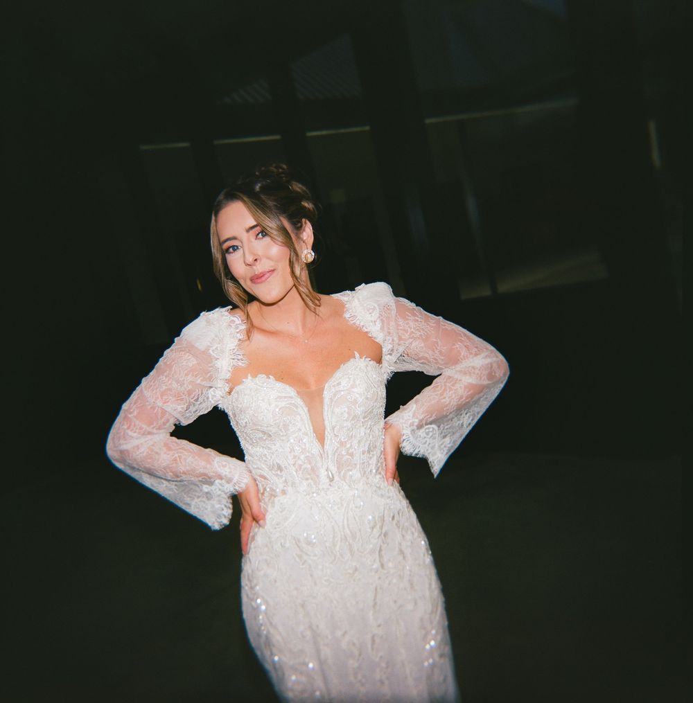 A figure in a sparkly white lace dress with sheer sleeves poses against a dark background.
