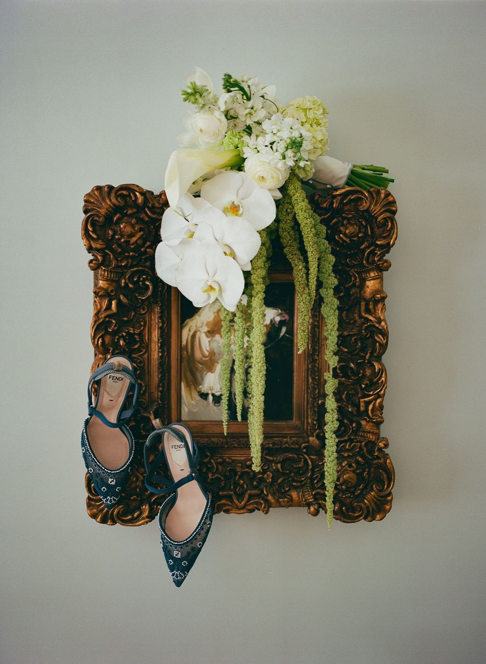 Elegant blue flats displayed next to ornate gold mirror with white orchids and greenery arrangement on wall.