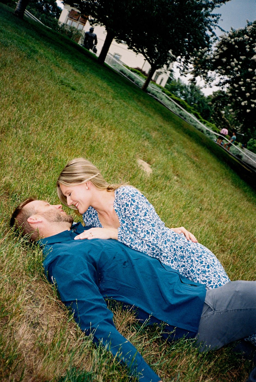 A sequence of photos shows two people playfully falling backwards onto a grassy lawn on a sunny day.