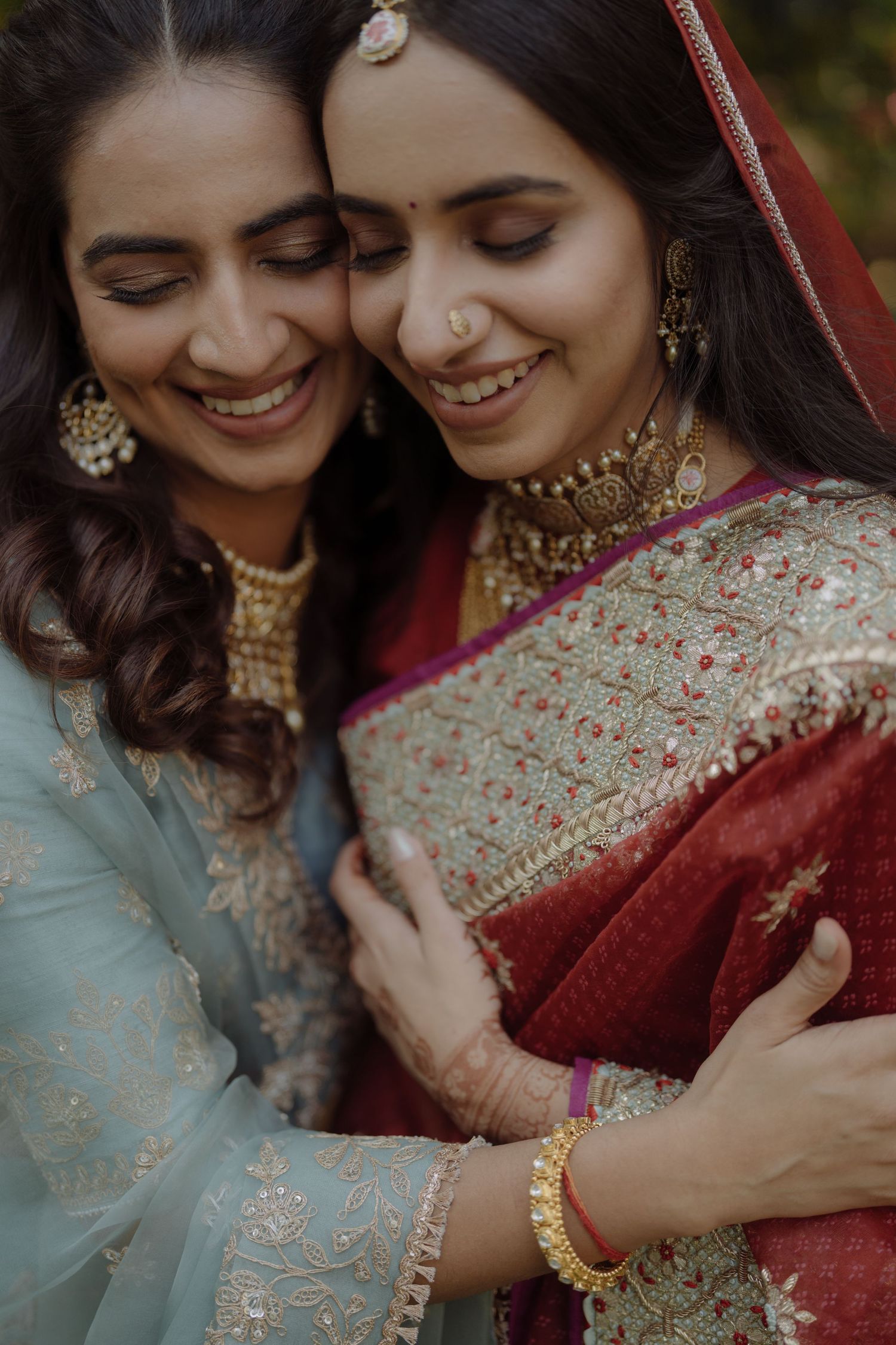 Two women in traditional Indian attire share an intimate moment wearing jewelry and embroidered clothing.