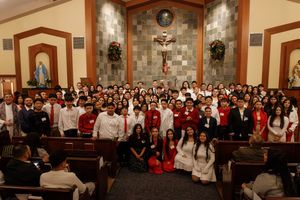 Large congregation gathered in a Catholic church interior with crucifix and religious statues visible in the sanctuary.