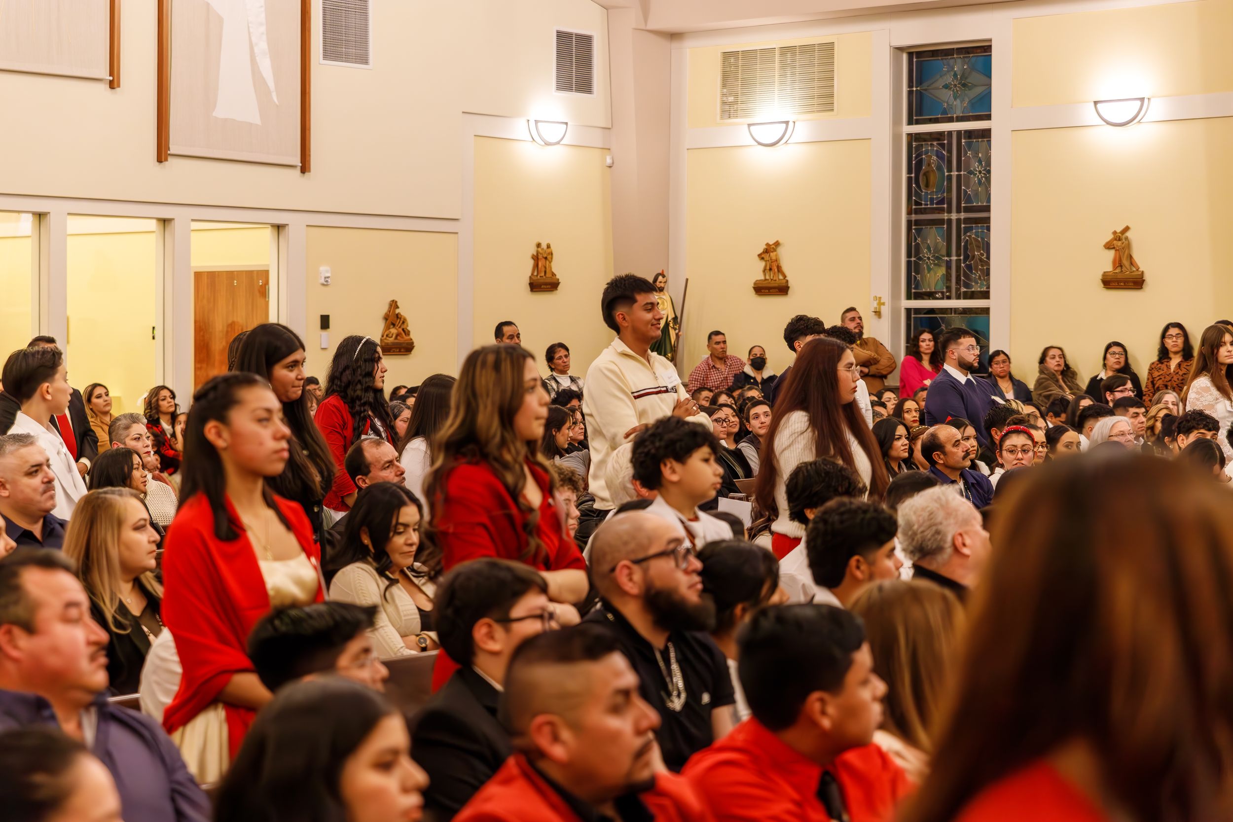 A large crowd of people wearing red and white attends an indoor event in a bright meeting room.