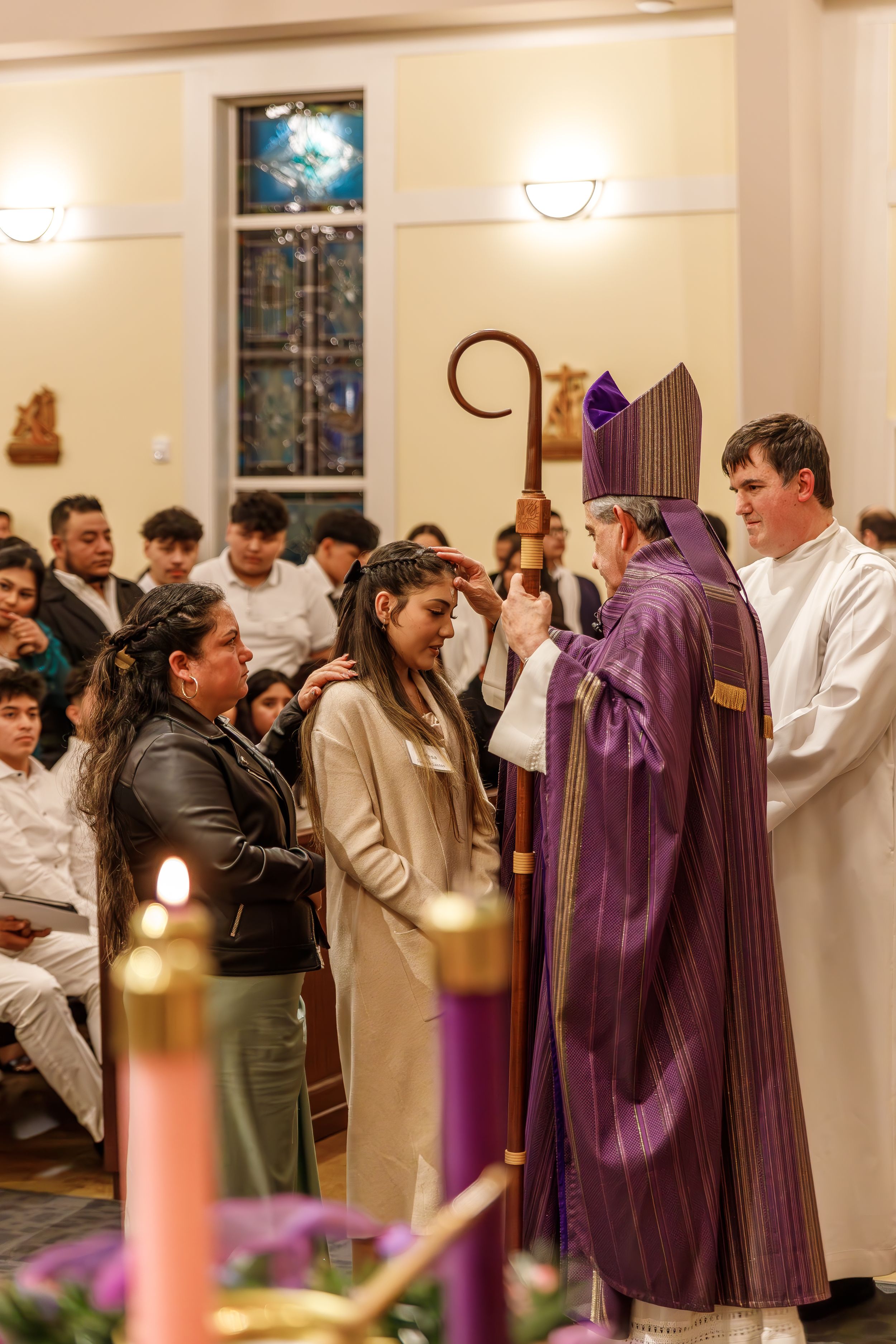 A religious ceremony takes place in a church with clergy members in purple vestments addressing gathered congregants.