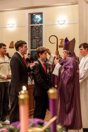 Religious ceremony in a church with candles and stained glass, featuring clergy in purple robes interacting with attendees.