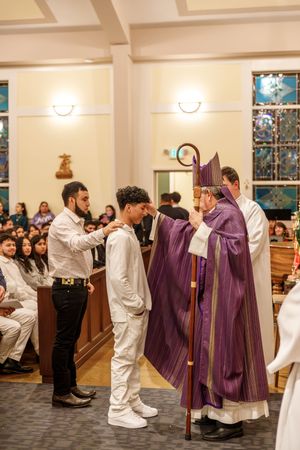 Catholic clergy in purple vestments performing a ritual at church with participants in white robes arranged in line.