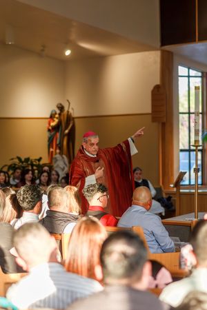 Interior view of religious service with congregation seated and clergy member in red robes standing.