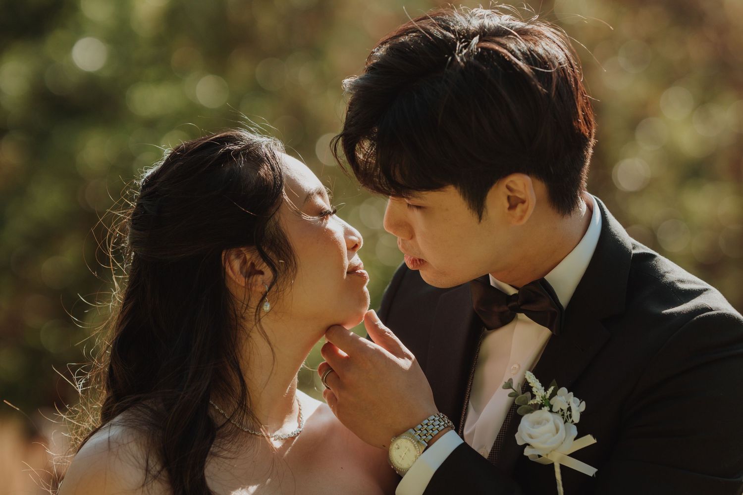 A couple in wedding attire shares a romantic moment at golden hour outdoors, the groom gently touching the bride's face. Victoria, BC.