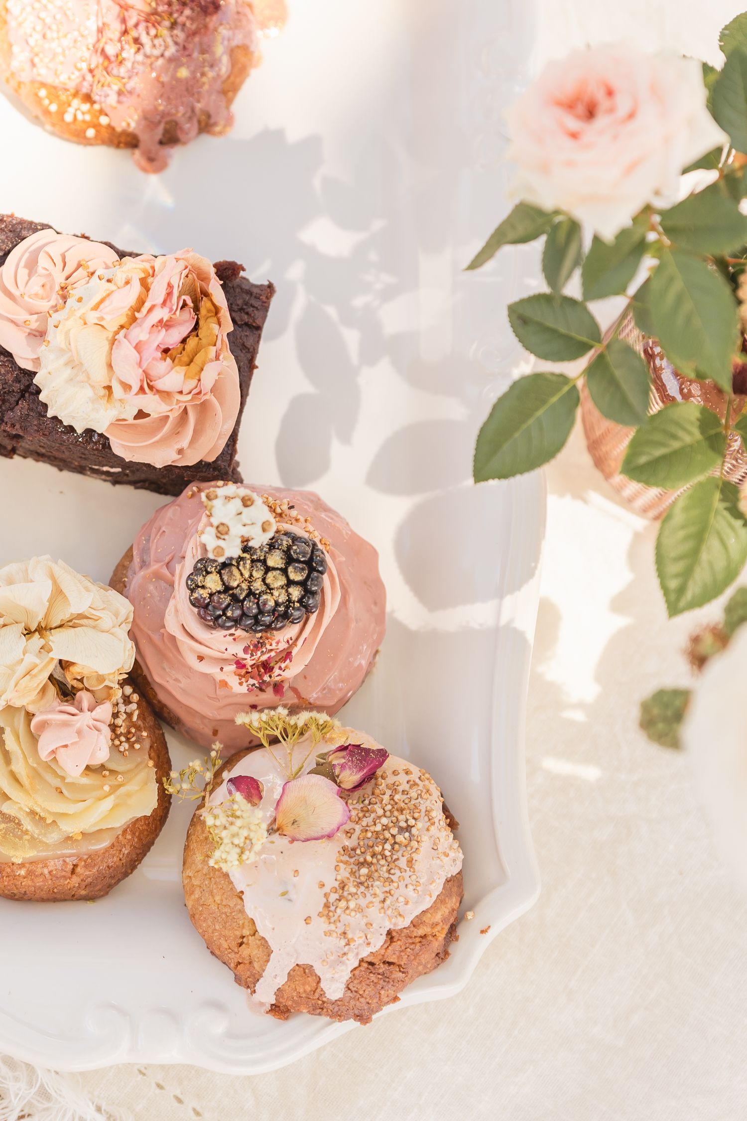 Elegant dessert display with pink roses and cream-topped pastries on white plates.