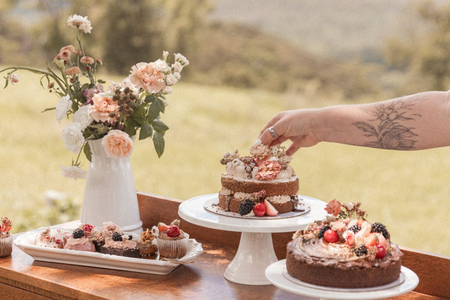 Collection of beautifully decorated cakes and desserts arranged on a rustic wooden table.