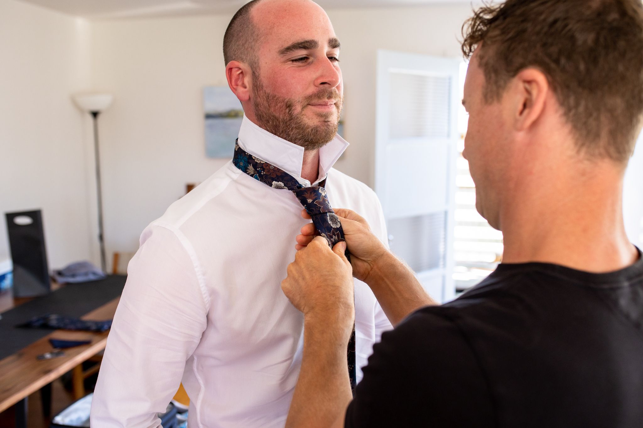 Best man helping groom adjust his tie while getting ready for wedding.