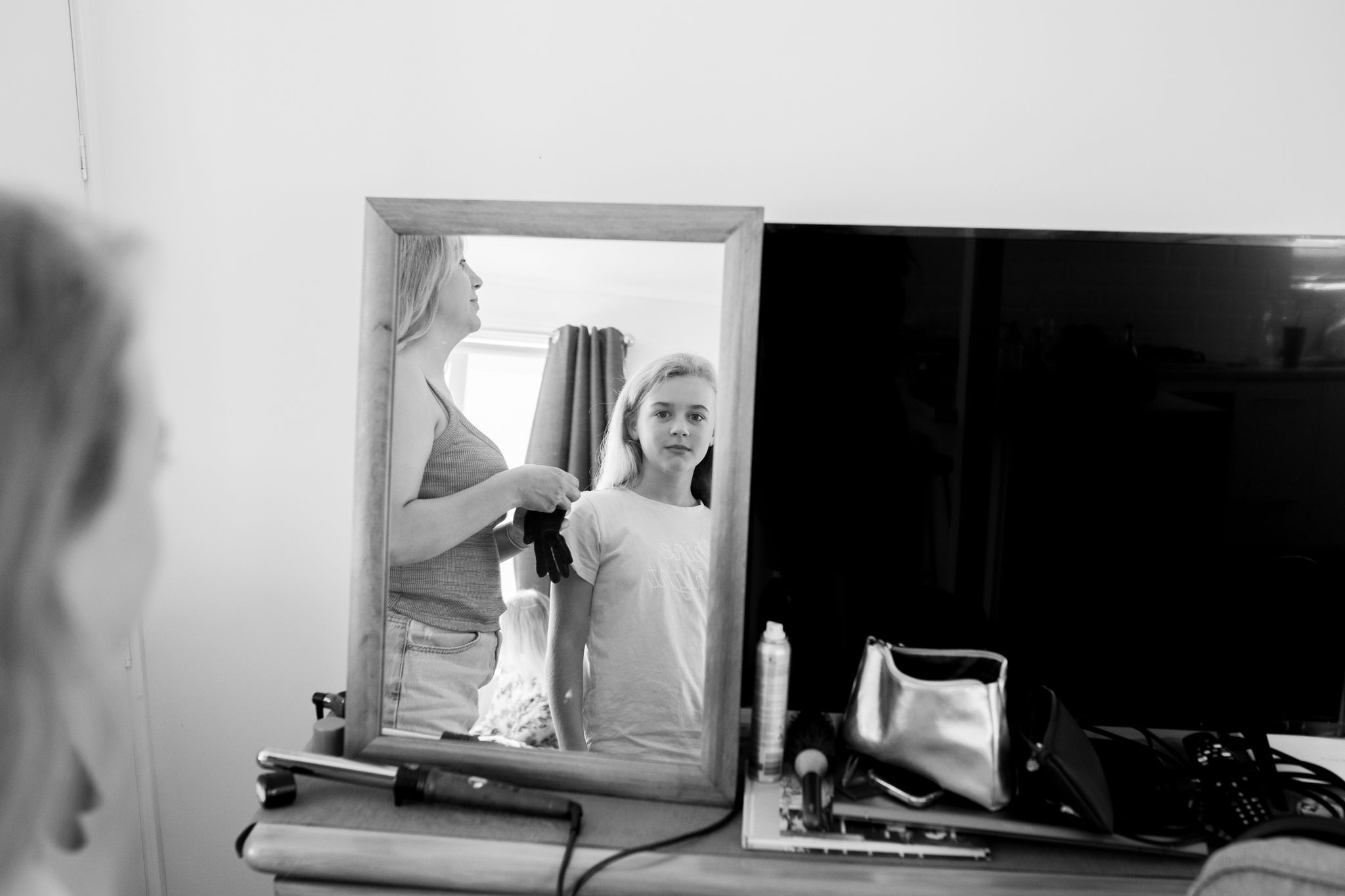 Black and white reflection of person styling hair in bathroom mirror.
