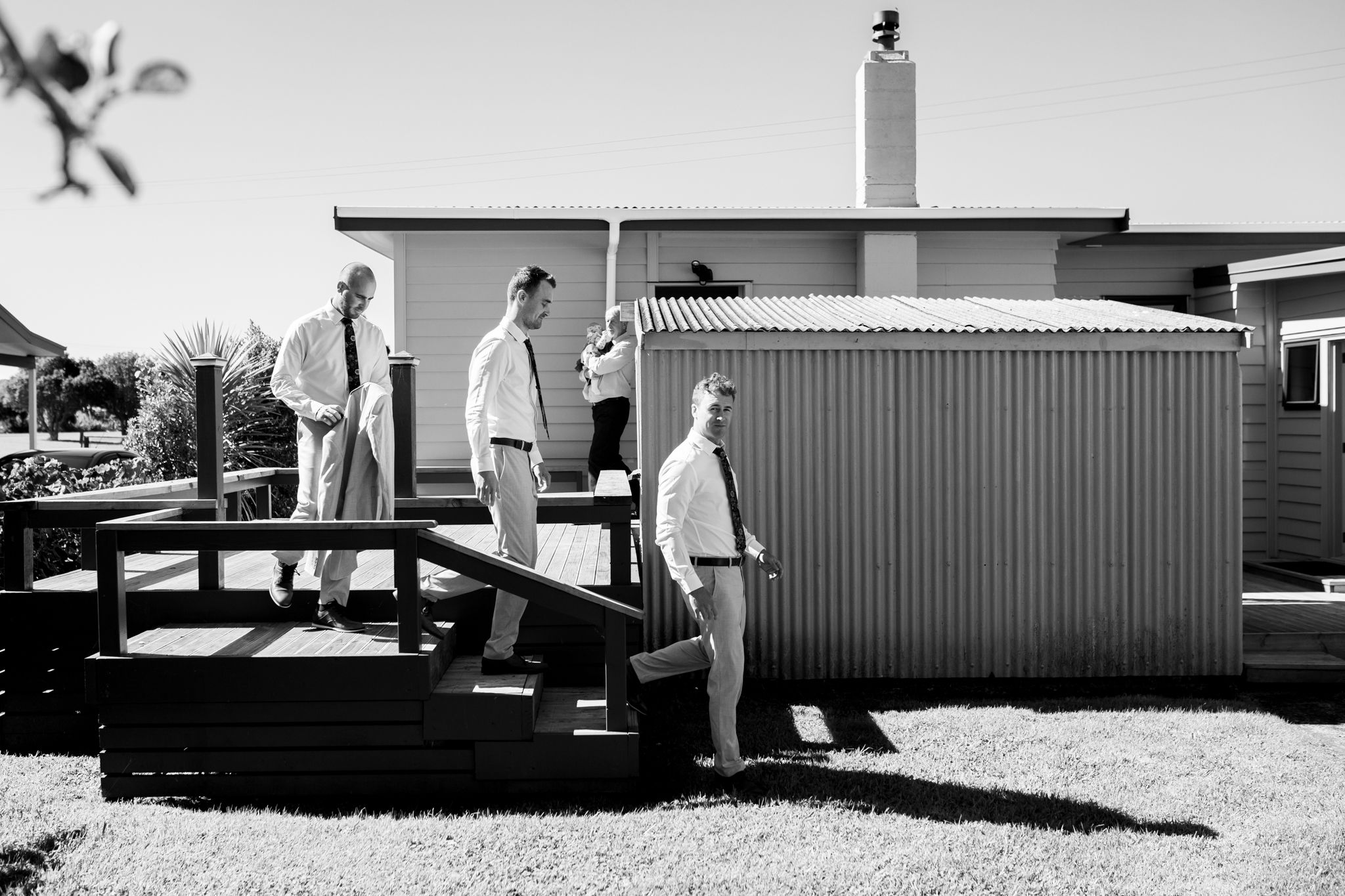 Three people standing on a wooden deck outside a building in black and white photography.