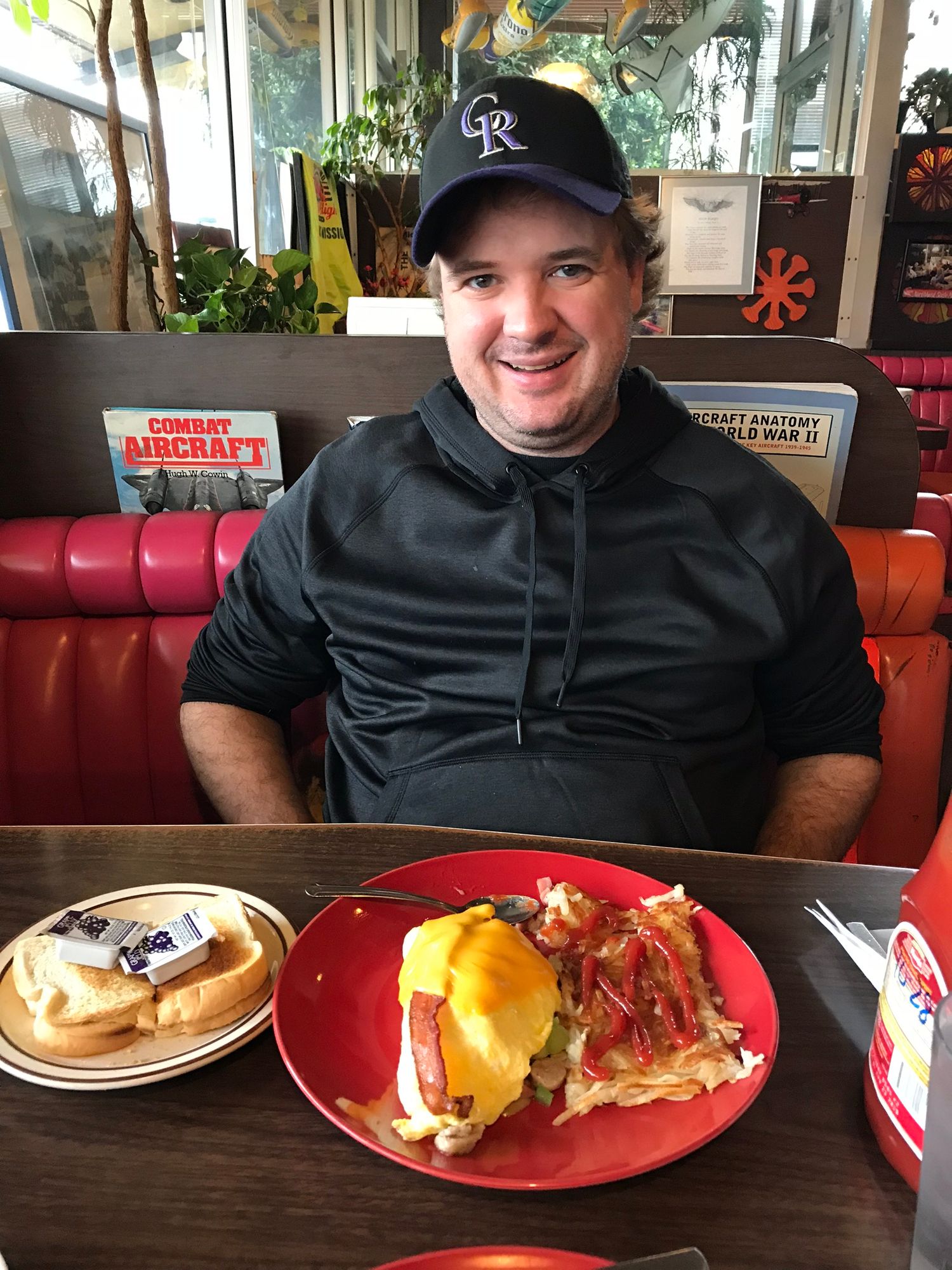 Diner customer seated with eggs benedict breakfast plate and baseball cap at restaurant booth.
