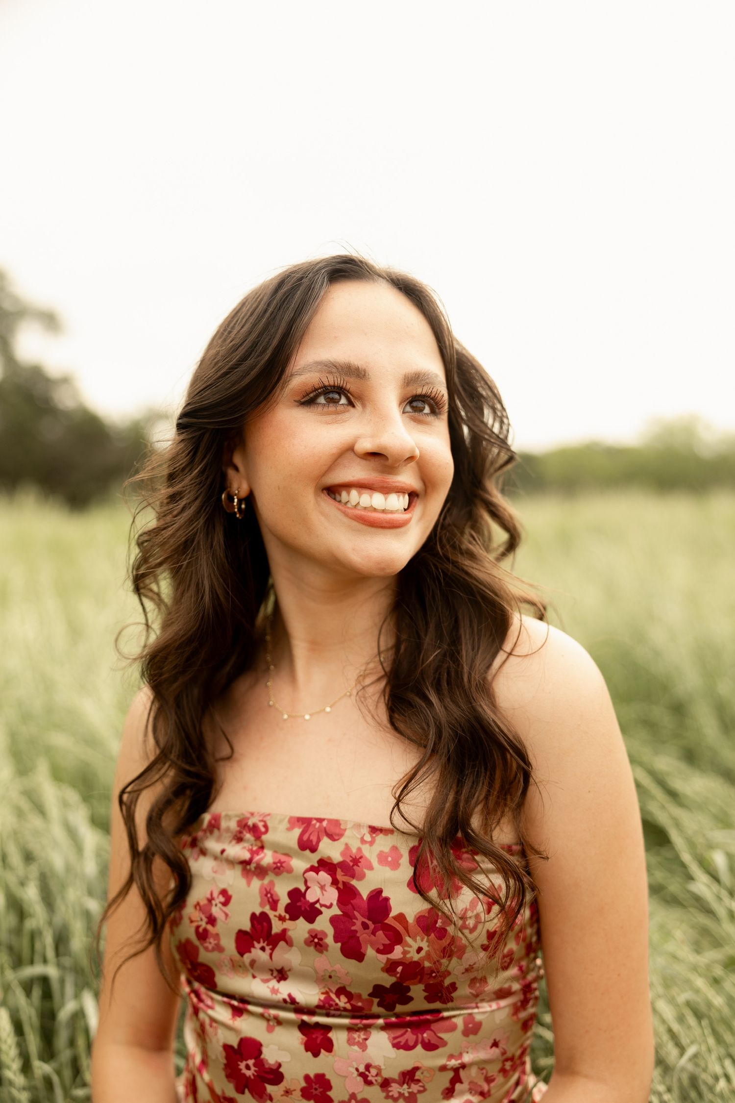 Woman in floral dress smiles in field during sunset portrait session.