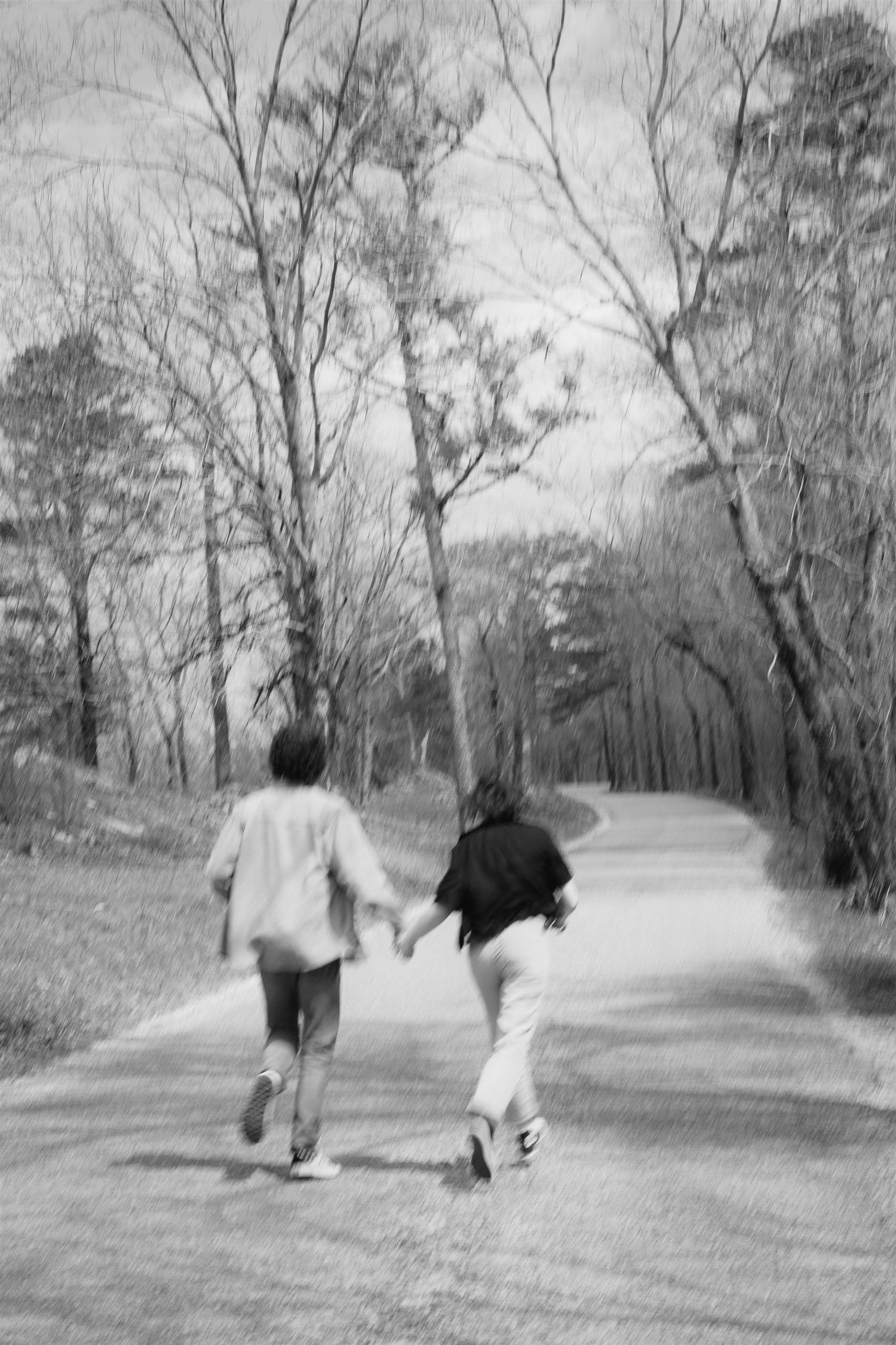 Black and white engagement photo running down road, Adventurous couple session in the woods, Motion blur romantic photo in nature.