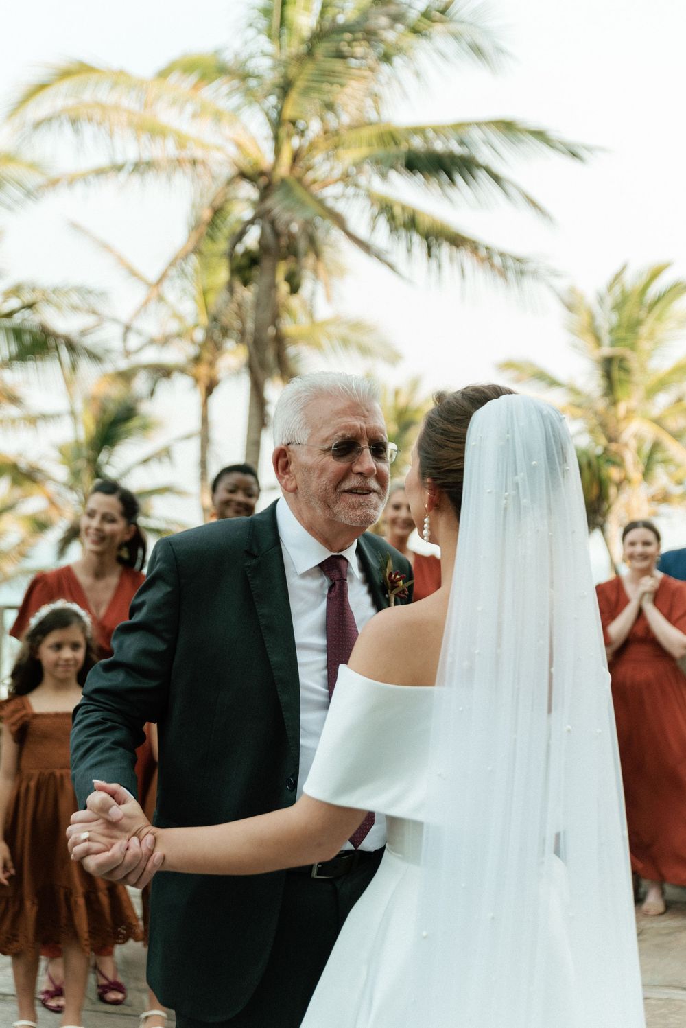 Bride and older man share a father-daughter dance outdoors near palm trees at a tropical beach wedding.